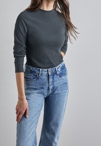 Mörkgrå ribbade långärmade topp i kombination med ljusblå högmidjade jeans med klassisk femficksdesign och lätt slitage.