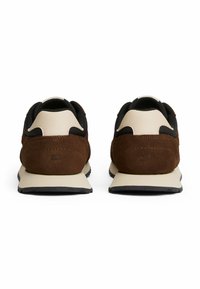 Zapatillas de gamuza marrón y malla negra con una suela de goma crema, que presentan una textura suave y un diseño minimalista, vistas desde la parte trasera.