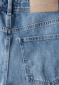 Vaqueros de jean de color azul claro con un bolsillo trasero y detalles cosidos, con una etiqueta de cuero beige que dice "STREET ONE - DENIM ATELIER."