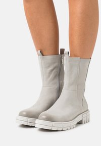 Bottes à chevilles grises avec une finition en cuir lisse, une fermeture éclair latérale et une semelle blanche épaisse avec un motif de bande de roulement texturé.