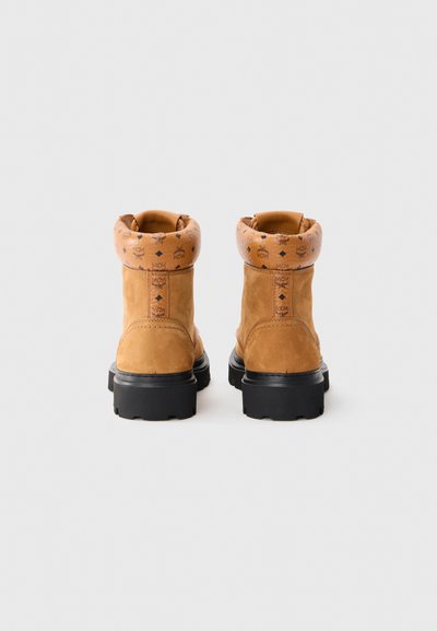 Tan suede ankle boots with a black rubber sole, featuring a patterned tan cuff and stitched detailing on the heel and sides.