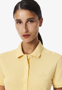 Polo shirt jaune en coton texturé, avec un col classique, une patte de boutonnage et un logo brodé sur la poitrine gauche.