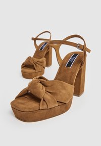 Paire de sandales compensées en daim marron avec talons blocs, brides cheville et un grand nœud noué sur les brides avant.