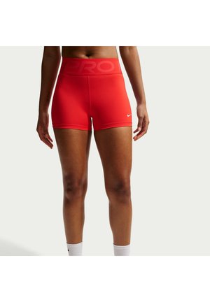Kvinde iført lyse røde atletiske kompressionsshorts med "PRO" taljebånd og lille hvid Nike-logo på venstre lår, stående mod en ensfarvet baggrund.