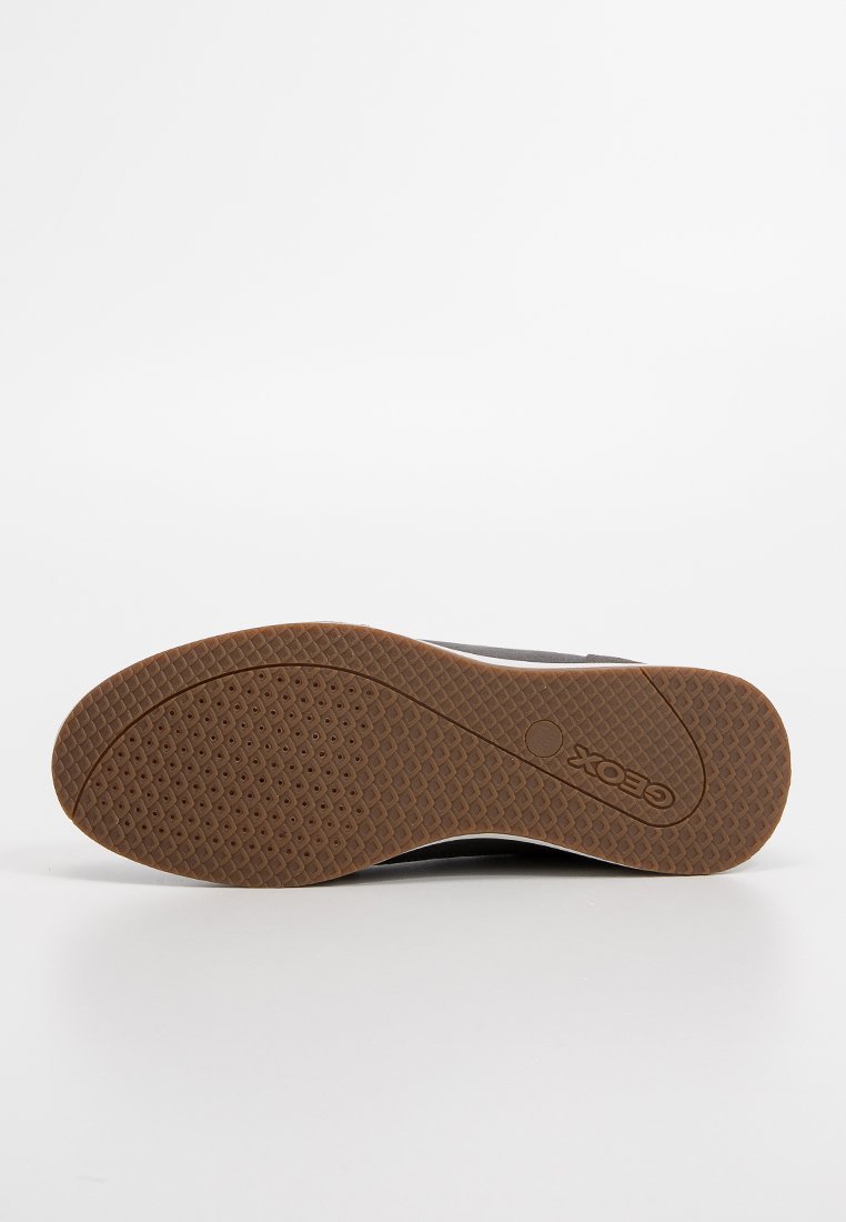 Semelle de chaussure avec une grip en caoutchouc texturé brun, motif de bande de roulement circulaire et logo de la marque Geox embouti près du talon sur fond blanc.