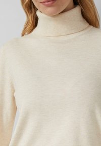 Maglione a collo alto di colore crema realizzato in morbido materiale a coste, con un collo alto e silhouette aderente. Texture liscia con leggere variazioni.