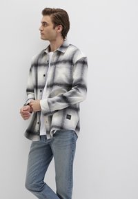 Black and white plaid flannel shirt with a relaxed fit, featuring large checks, button closure, and a label on the hem, paired with blue jeans.