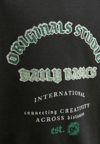 Felpa nera con testo audace ricamato in verde e argento, con frasi come "Originals Studio" e "Daily Basics."