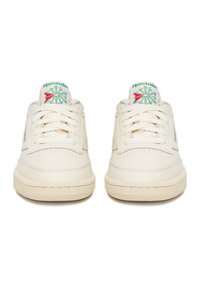 Pár krémovo bielych tenisiek Reebok s krémovými šnúrkami, textúrovanou podrážkou a zeleno-červeným logom na jazyku, pohľad spredu.