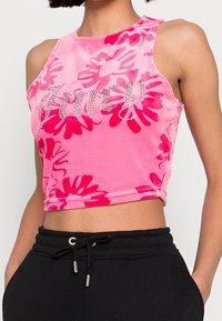 Rosa ärmlös crop top med röd blommönster och rhinestone-texten "True" som bärs med svarta dra-på-byxor.