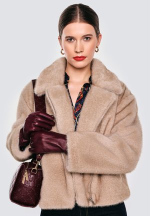 Beżowa kurtka z futerka ekologicznego z szerokim kołnierzem, zestawiona z bordowymi skórzanymi rękawiczkami i pasującą torebką o teksturowanym wzorze.