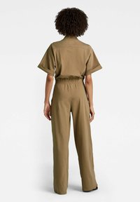 Khaki overálek s krátkými rukávy, elastickým pasem a širokými nohavicemi. Hladká tkanina, minimalistický design, bez výrazných vzorů nebo ozdob.