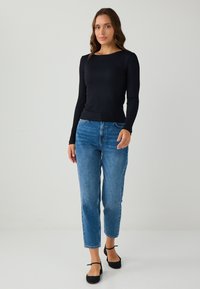 Schwarzes, geripptes Langarmoberteil kombiniert mit hellblauen, hochgeschnittenen, geraden Jeans. Schwarze Ballerinas mit Knöchelriemen. Glatte, enganliegende Texturen.