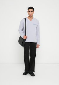 Gaiši purpura v-veida svīteris mīkstā adījumā, apvienots ar melniem brīvi pieguļošiem biksēm un melniem apaviem. Melnā sūtītāja soma karājas no pleca.