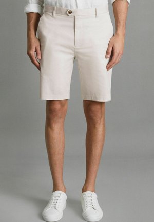 Beige shorts van katoenmix, perfecte pasvorm, sluiting met knopen aan de voorkant en zijzakken. G gedragen met witte veterschoenen.