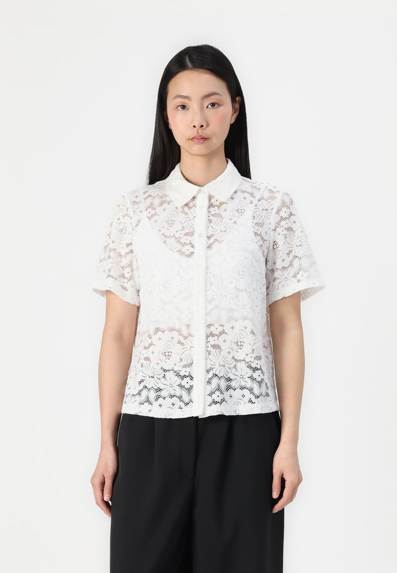 White lace blouse with short sleeves, featuring a collared neckline and floral patterns. Fabric has a sheer, textured appearance.