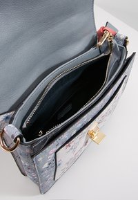 Blue floral-patterned handbag open to show inner zipped compartment and gold-tone clasp with leather lining and fabric interior pockets.