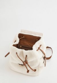 Bolso tipo cubo blanco de textura suave con cierre de cordón de cuero marrón y detalles en cuero marrón. En el interior cuenta con un bolsillo marrón.