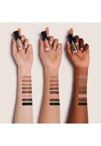 Drie handen die lipproducten met zwarte doppen vasthouden. Daaronder swatches van verschillende nude tinten op armen met verschillende huidskleuren.