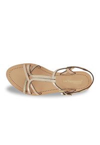 Sandalia plana de cuero dorado con tiras entrelazadas y hebilla ajustable en el tobillo. Detalles texturizados en las tiras.