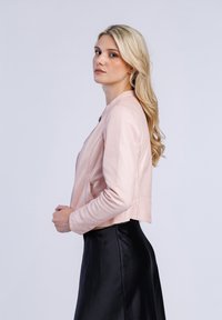 Lichtroze leren bomberjack met een ronde halslijn en rits, gecombineerd met een zwarte satijnen rok. Glad textuur, cropped ontwerp.