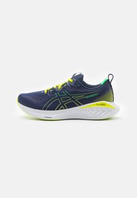 Scarpa sportiva blu navy con tomaia in rete, lacci giallo neon e dettagli verdi. Presenta una suola bianca imbottita con un motivo testurizzato.