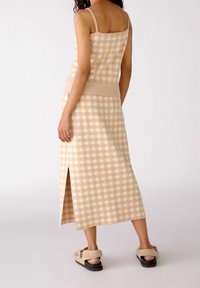 Top de punto de cuadros en color beige con tirantes finos, combinado con una falda a la altura del tobillo que presenta una abertura lateral y una cinturilla texturizada. Material suave.