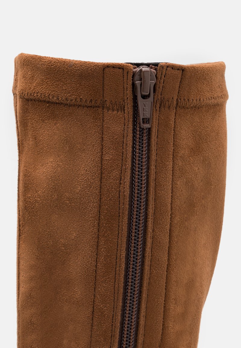 Bruine suède kniehoog laars met een ritsluiting, horizontale stiksels en een gladde textuur op de buitenste schacht.