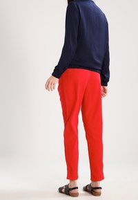 Marinblus med lång ärm och texturerad yta, matchad med röda slim-fit byxor. Skorna har svarta remmar och en träsoff.