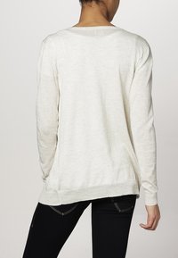 Světle béžový svetr vyrobený z měkké pleteniny. Dlouhé rukávy, volný střih s širokým výstřihem a žebrovaným lemem. Minimalistický design.