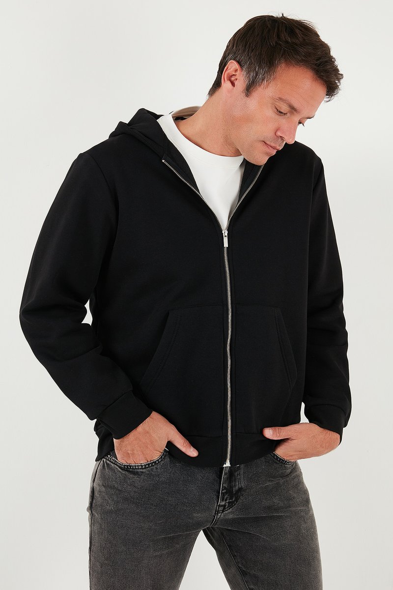 Crna zip-jakna od mekog materijala. Sadrži prednji džep, rebraste rukave i kapuljaču s vezicom. Nošena preko bijele majice.