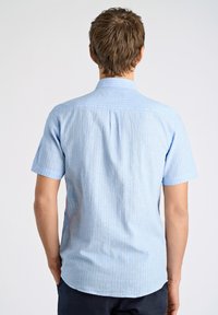 Lichtblauw kortomlaag shirt met verticale witte strepen, kraag en details met een rugplooibroek. Katoenen materiaal met een gladde textuur.