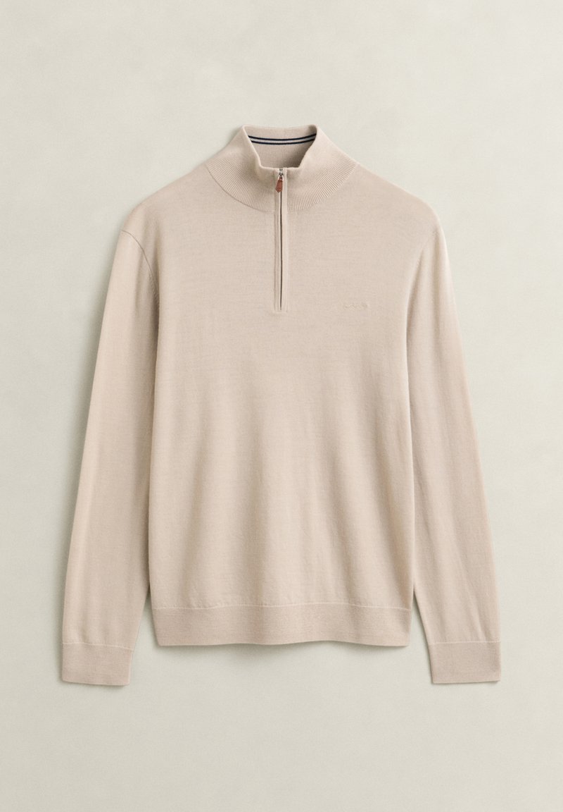 Beige trui met lange mouwen, geribde hoge kraag en korte rits aan de voorkant op een effen achtergrond.