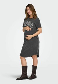 Hallist teksat kangendav raseduskleit lühikeste rullitud varrukatega, millel on sõna "ICONIC" valge niidiga. Sobitatud põlveni ulatuvate pruunide nahkkingadega.