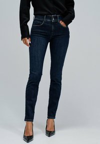 Vaqueros de mezclilla oscura con un diseño slim fit, que cuentan con un cierre clásico de botón y cremallera, bolsillos delanteros y una textura sutil.