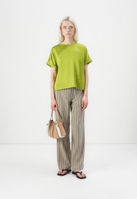 Lime green short-sleeve top, relaxed fit; paired with beige-and-brown striped trousers. Accessory: small handbag in neutral tones, with braided handles.
