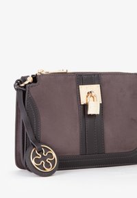 Portafoglio in suede grigio e pelle nera con un'accattivante chiusura a lucchetto dorato, caratterizzato da un charm rotondo e una dettagliata cucitura a contrasto. Chiusura con cerniera.