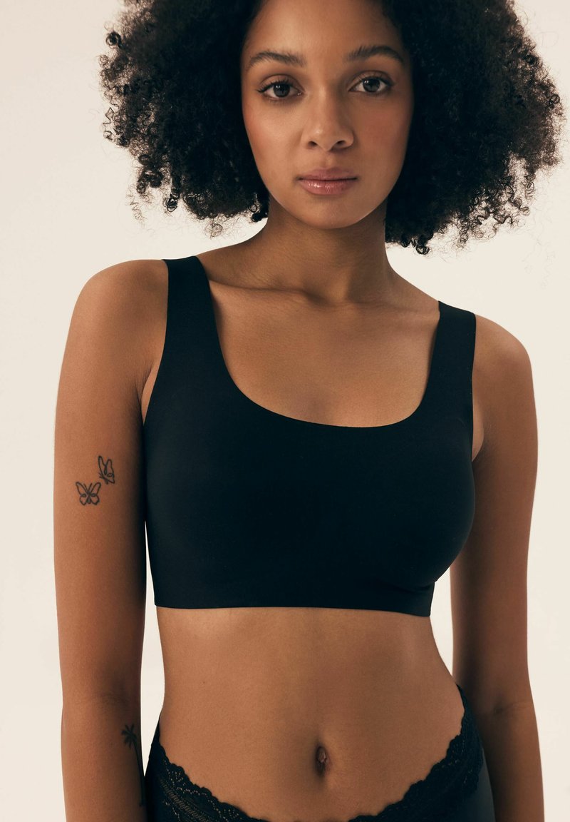 Schwarzer nahtloser Bralette mit Rundhalsausschnitt und breiten Trägern; weicher, elastischer Stoff; getragen mit Unterwäsche mit Spitzenakzenten.