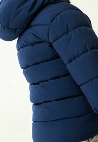 Doudoune bleu marine avec un design matelassé, dotée d'une capuche et d'un rembourrage épais pour l'isolation. Coutures visibles et texture de tissu lisse.