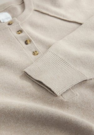 Beige strikket pullover med henley-krave, der har tre brune knapper og ribbede mansjetter. Blød tekstur og et afslappet design.