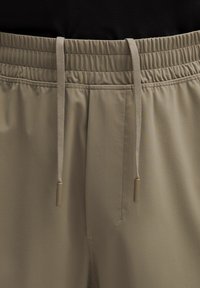 Beige joggerbroek met een elastische tailleband en trekkoord, voorzien van zijzakken. De stof is glad met een subtiele matte afwerking.