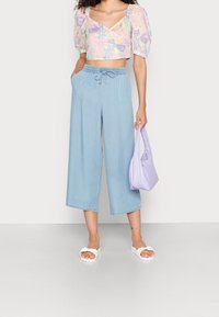 Crop top floral léger avec des manches ballon dans des couleurs pastel, accompagné d'un pantalon en denim large et léger de couleur bleu clair, et d'un sac à épaule lavande.