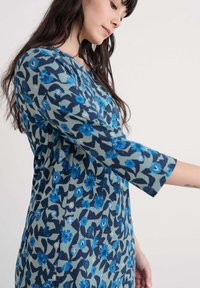 Rochie florală dintr-un material de bumbac moale, cu flori albastre pe un fundal verde, cu mâneci trei sferturi și guler rotund.