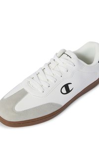 Zapatilla blanca con detalles en ante gris, suela de goma texturizada y logo negro. Cuenta con cordones y un diseño de punta redondeada.
