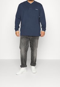 Marineblauwe longsleeve polo met een knoopsluiting en witte accentmanchetten. Draag het met een grijze spijkerbroek en witte sneakers. Calvin Klein-logo op de borst.