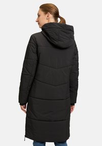 Cappotto lungo nero isolato con cappuccio, caratterizzato da un motivo trapuntato, cuciture verticali e tasche con zip per una maggiore funzionalità.