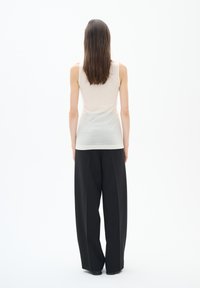 Vaaleanbeige tanktoppi, joka on yhdistetty mustiin leveälahkeisiin housuihin, esittelee rentoa istuvuutta ja sileää tekstuuria, nähtynä takaa.