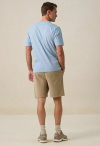 Lichtblauw shirt met korte mouwen en een ronde hals, gecombineerd met beige shorts. Zichtbare stikdetails en een ontspannen pasvorm.