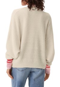 Krémový pletený svetr s volným střihem, který má nabírané rukávy a kontrastní pruhované manžety v růžové a červené barvě.