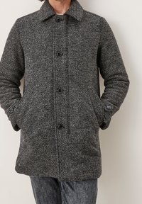 Abrigo gris de mezcla de lana con patrón de espiga, cuello vuelto, cierre frontal con botones y bolsillos laterales. Textura suave y ajuste entallado.